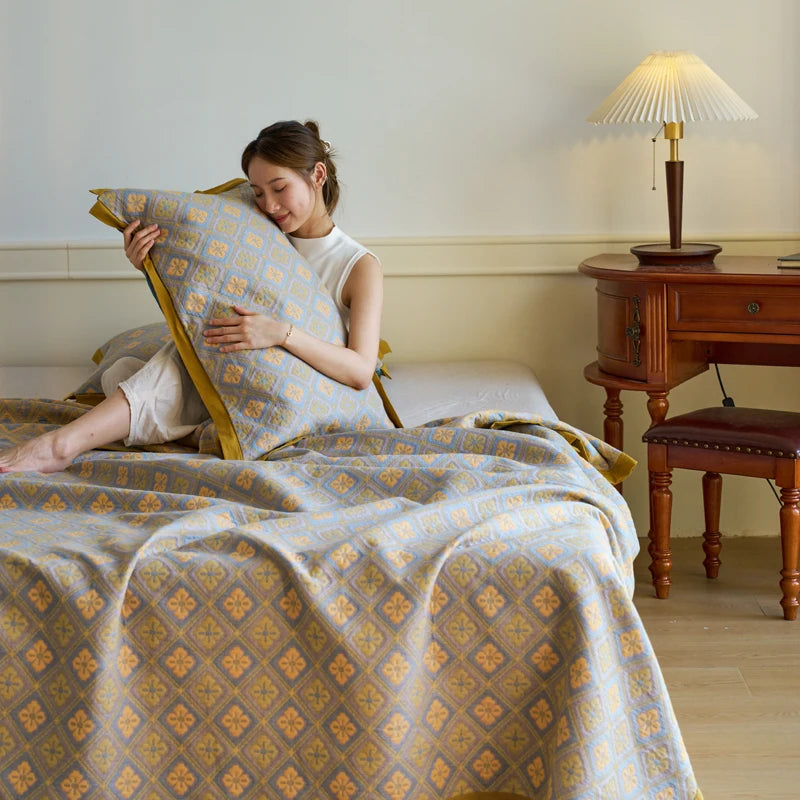 Woman sitting on a bed with patterned bedding in a room with wooden furniture and a lamp.