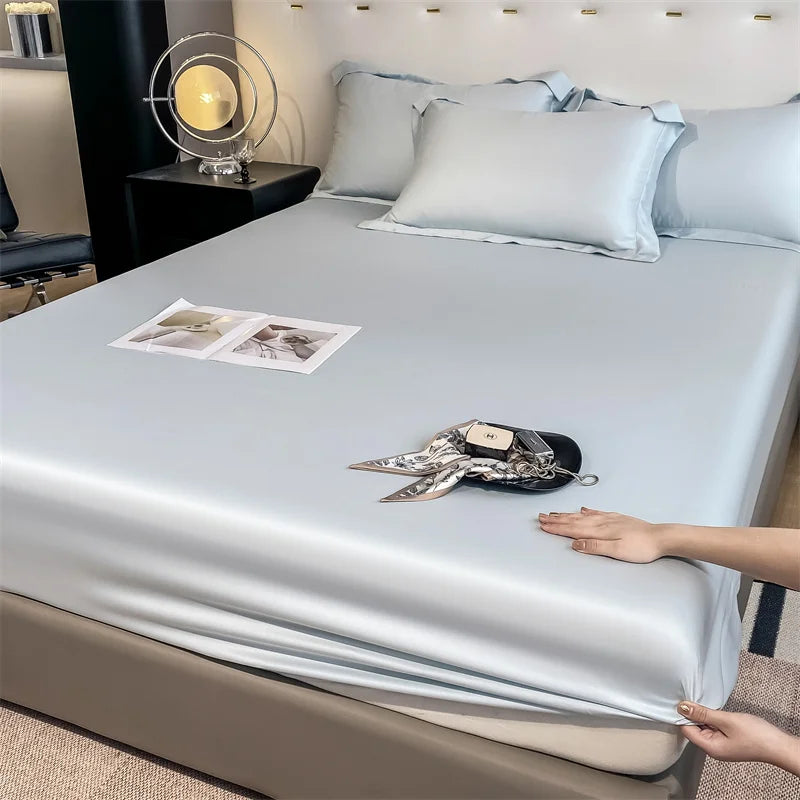 Person holding a satin sheet over a bed with decorative items on a nightstand.