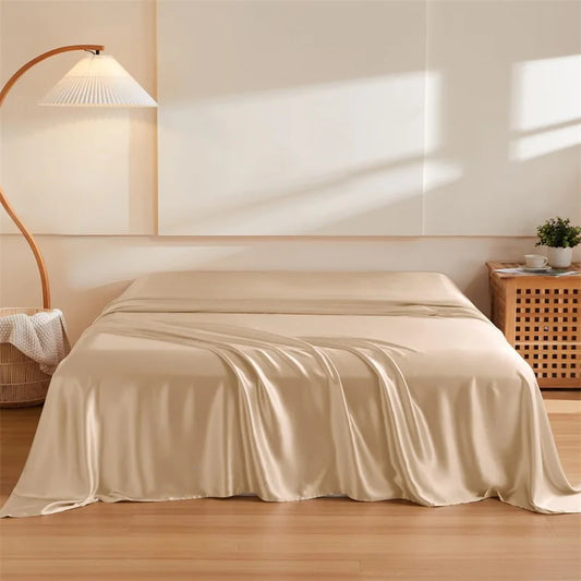 Beige satin sheet on a bed in a bedroom setting with a lamp and plant.