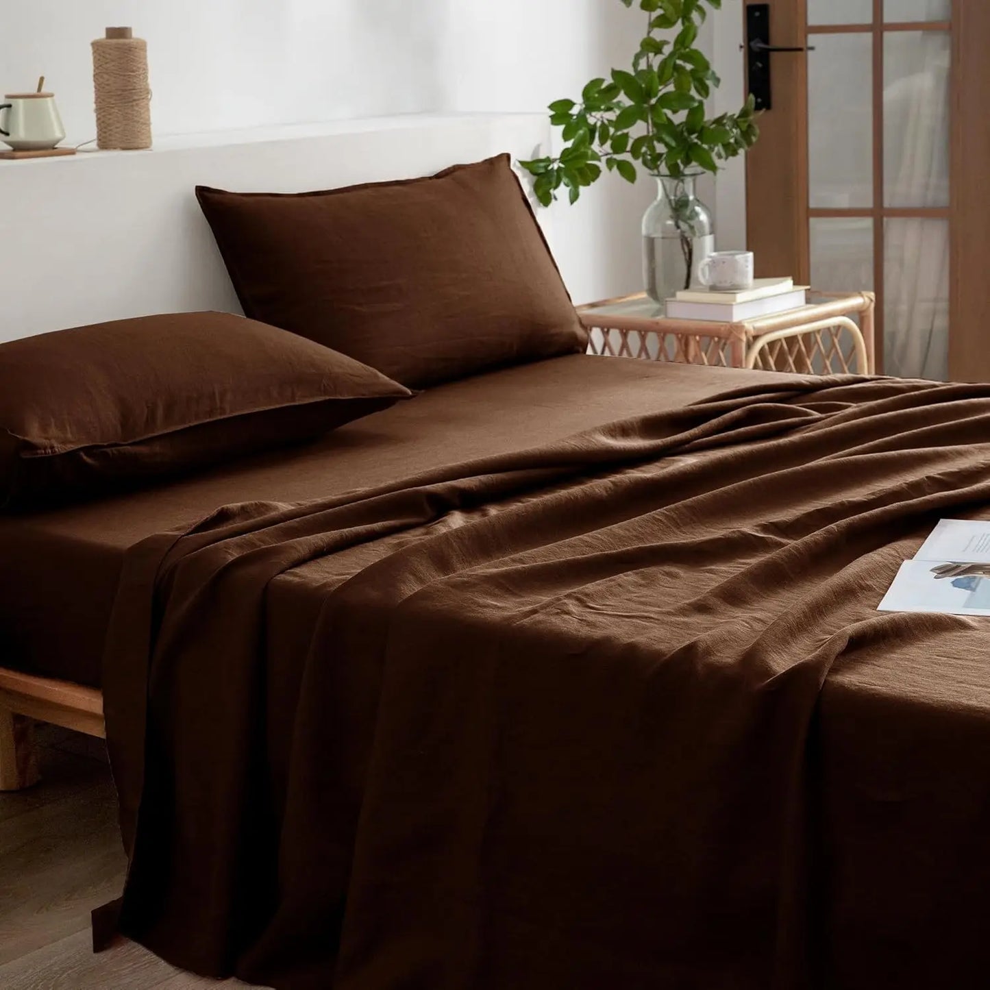Brown bedding set on a bed with a side table and plant in the background.