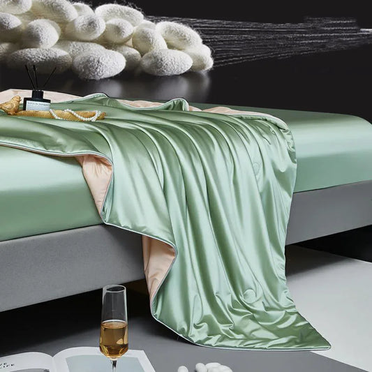 Green satin blanket draped over a bed with a glass of wine and book on a table.