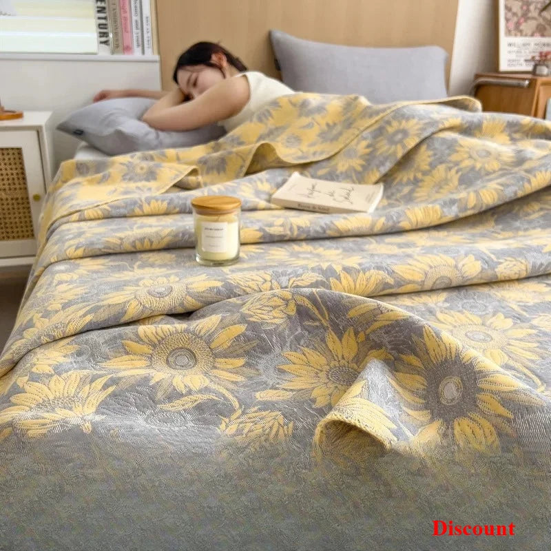 Woman lying on a bed with a yellow and gray floral patterned blanket, candle, and book.