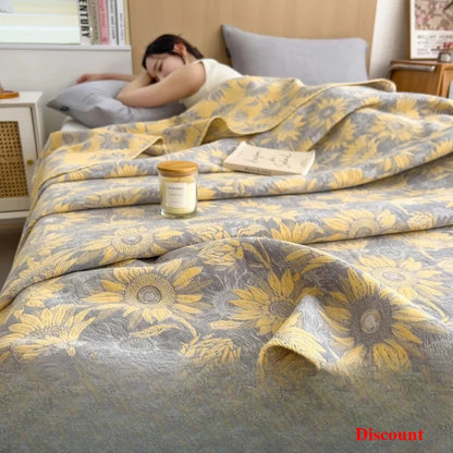 Woman lying on a bed with a yellow and gray floral patterned blanket, candle, and book.