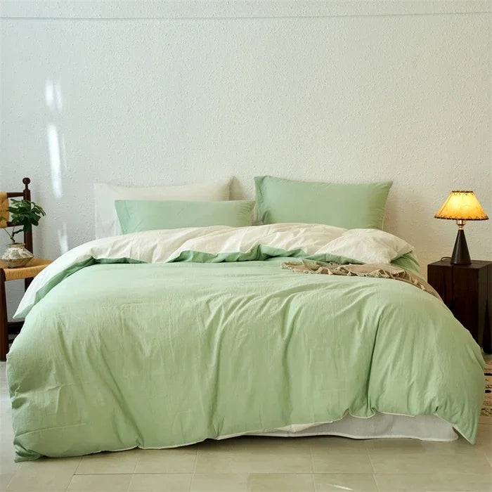 Bed with green bedding in a room with a lamp and small table.