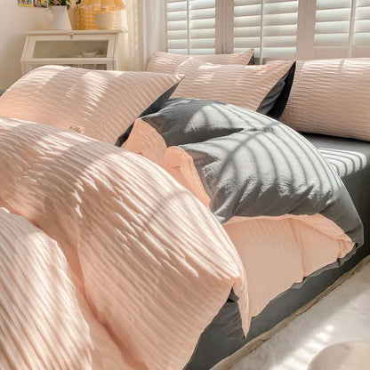 Neatly made bed with pink and gray bedding in a well-lit room.