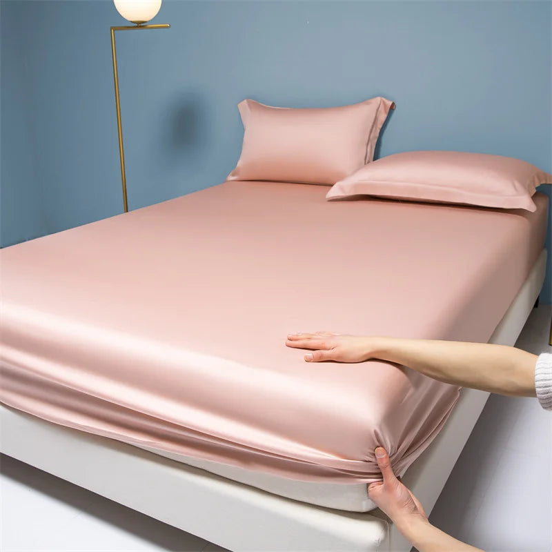 Pink satin sheet set on a bed with a hand touching it, against a blue wall.