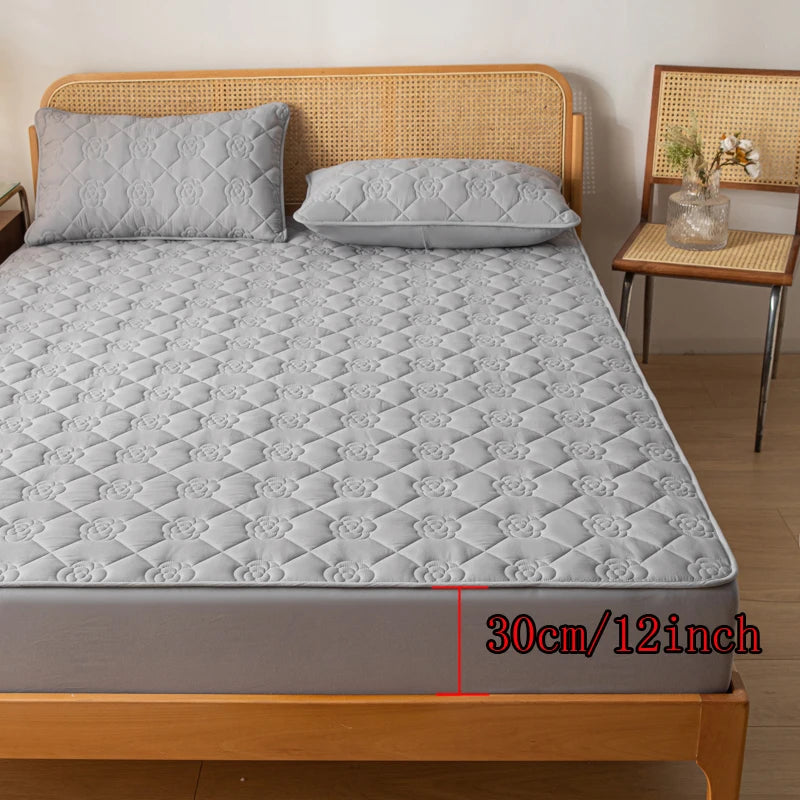 Gray quilted mattress cover on a bed with wooden headboard and side table.