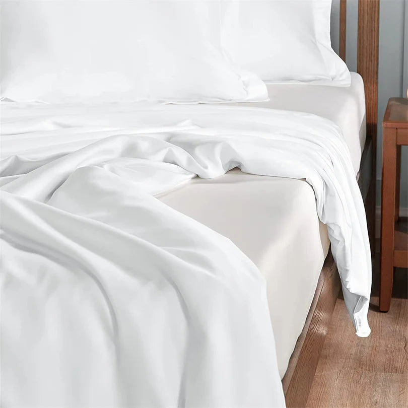 White bed sheets and pillowcases on a bed with wooden bedside table.