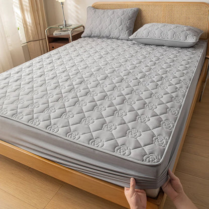 Gray quilted mattress cover being fitted onto a bed in a bedroom setting.