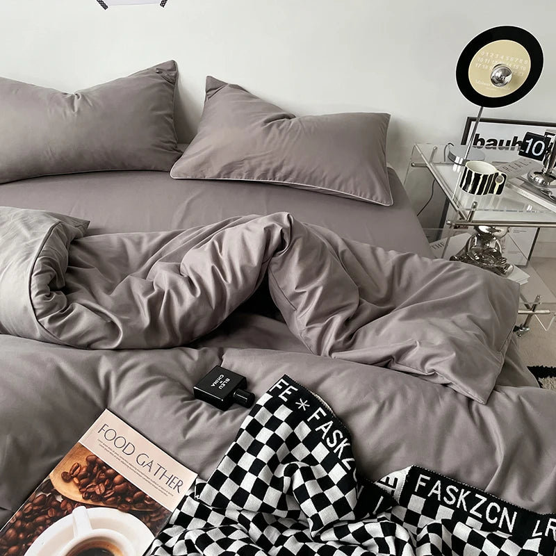 Gray bedding set on a bed with a checkered blanket and books, in a room setting.