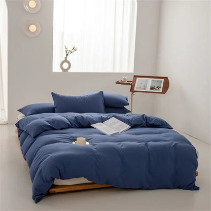 Blue bedding set on a bed in a minimalistic room with a window and lamp.