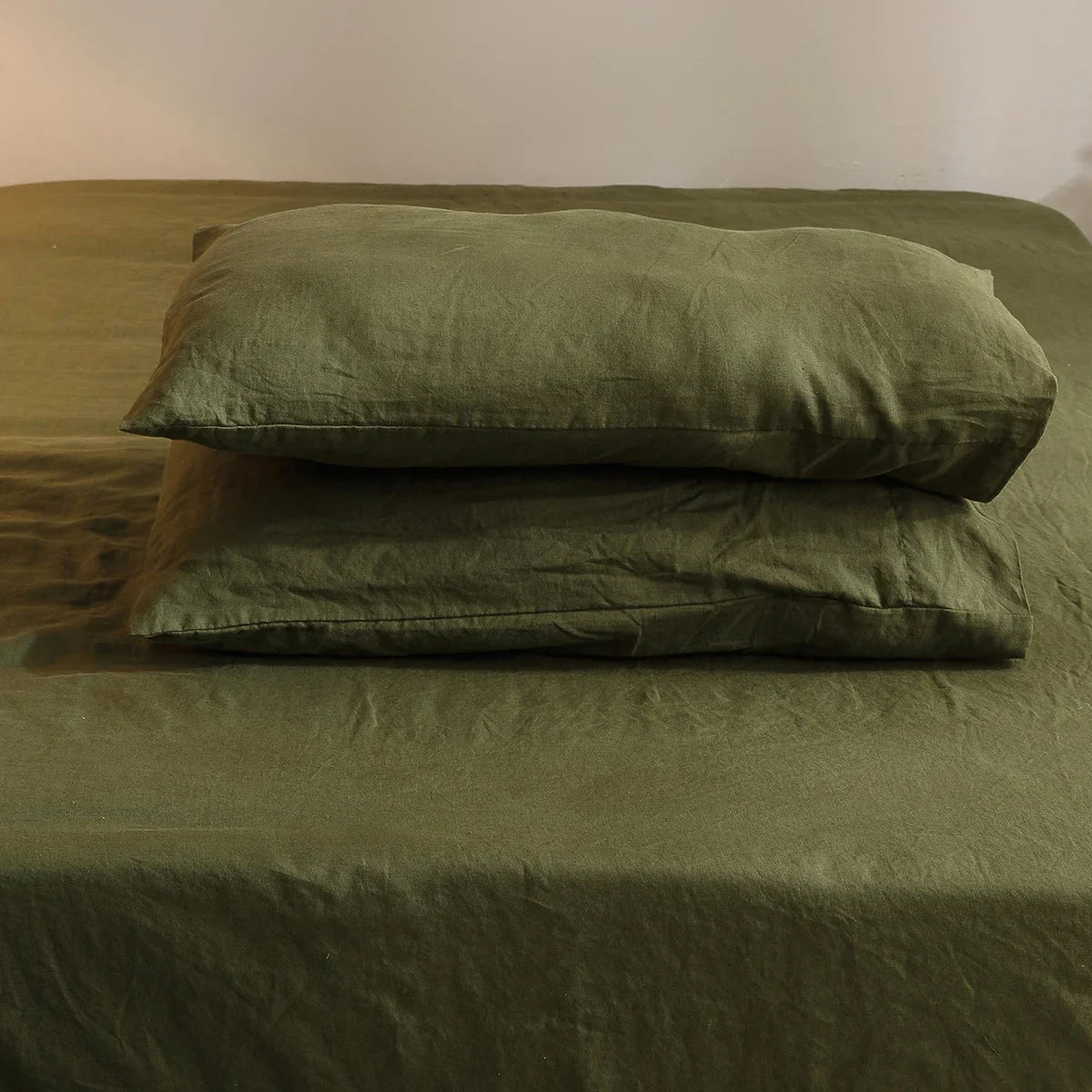 Green bedding set with a pillow on a bed against a plain wall.