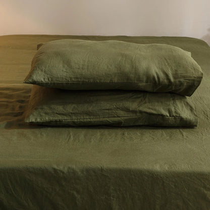 Green bedding set with a pillow on a bed against a plain wall.