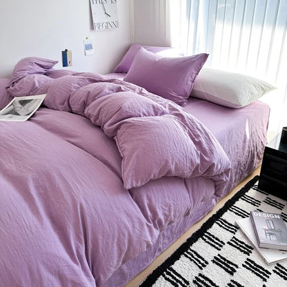 Bed with purple bedding and pillows in a bedroom setting.