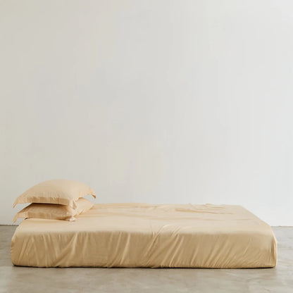 Beige bed sheets and pillows on a bed against a plain wall.