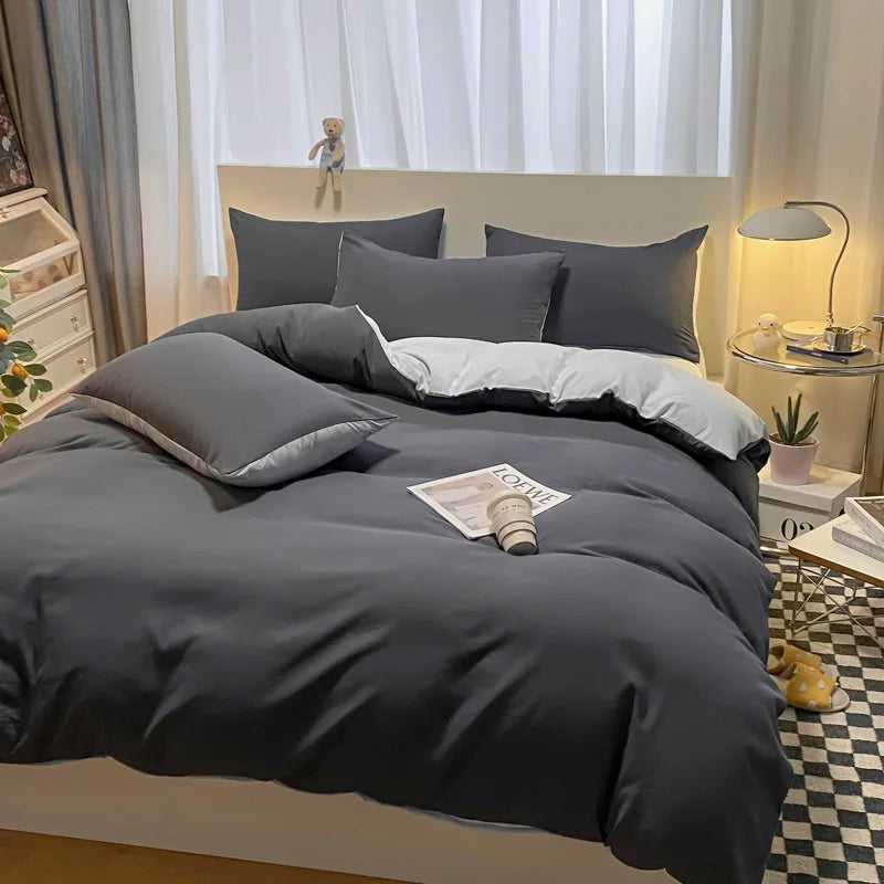 Gray bedding set on a bed in a bedroom with a lamp and window in the background.