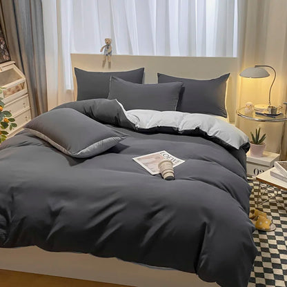 Gray bedding set on a bed in a bedroom with a lamp and window in the background.
