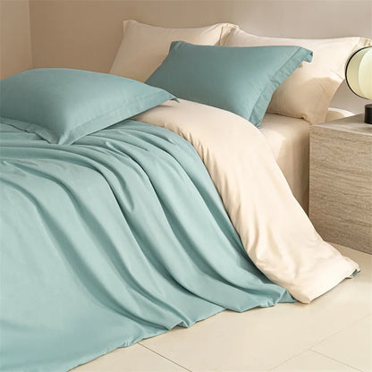 Teal bedding set on a bed with beige pillows and a lamp in the background.