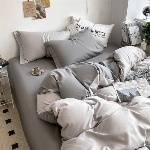 Gray bedding set on a bed with pillows and a newspaper.