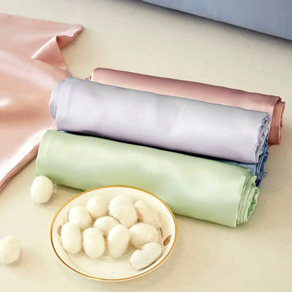 Rolls of pastel-colored fabric stacked with a bowl of white balls on a light background