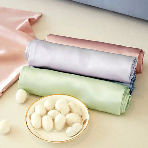 Rolls of pastel-colored fabric stacked with a bowl of white balls on a light background
