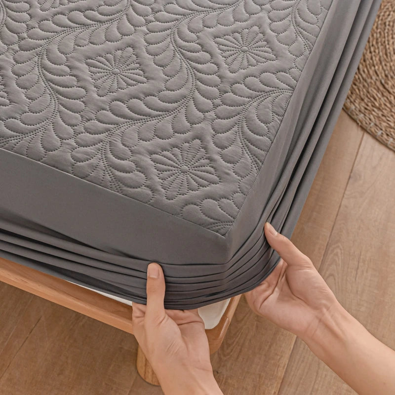 Person holding a gray quilted mattress protector on a wooden bed frame.