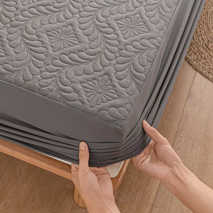 Person holding a gray quilted mattress protector on a wooden bed frame.