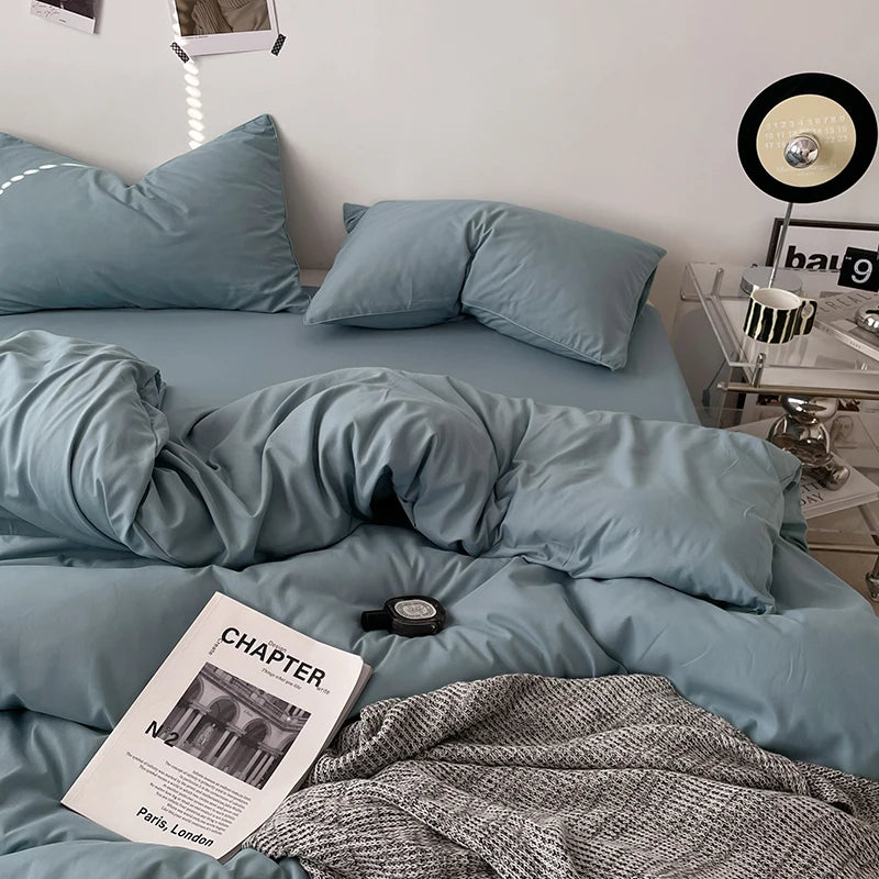Blue bedding set on a bed with a magazine and lamp in the background