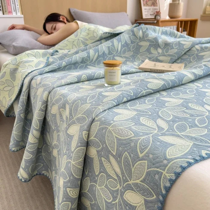 Person lying in bed under a floral-patterned blanket with a candle and book on the pillow.