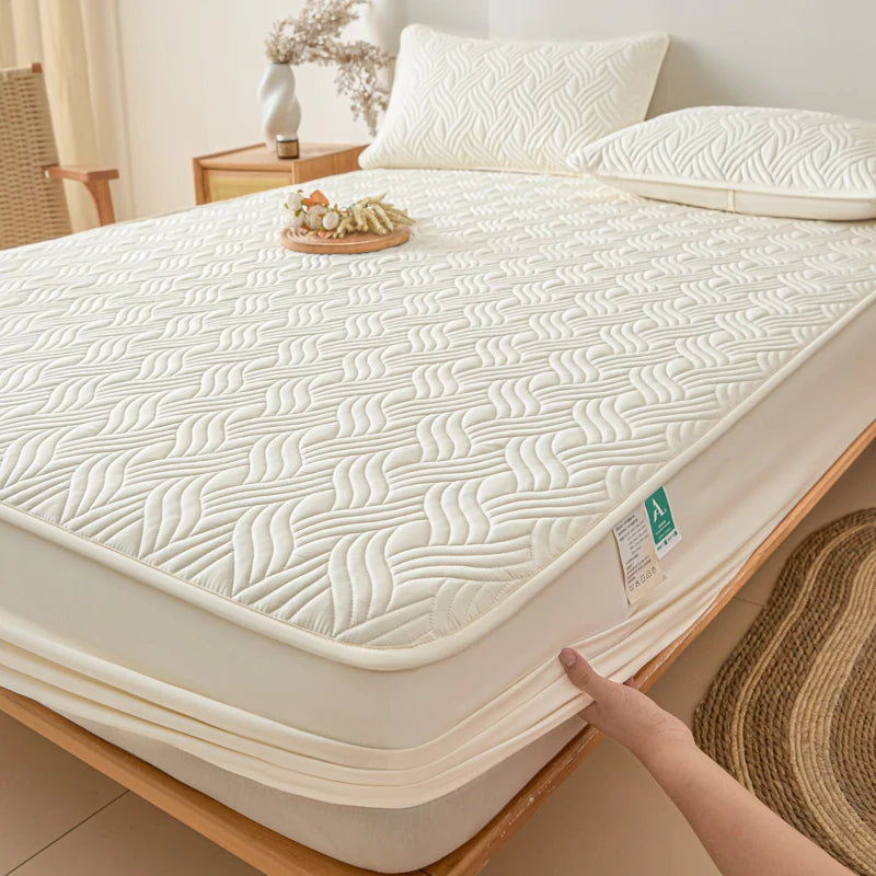 Beige mattress cover on a bed with a hand touching it, in a bedroom setting.
