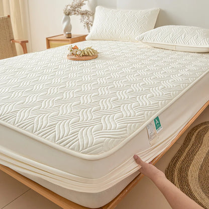 Beige mattress cover on a bed with a hand touching it, in a bedroom setting.