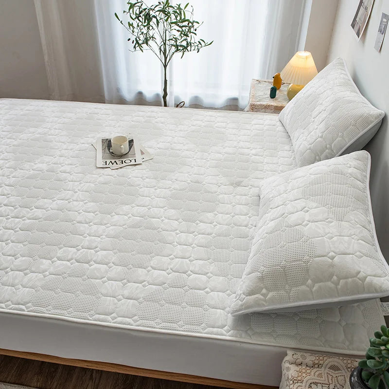 White quilted mattress cover on a bed with pillows and decor items in a bedroom.