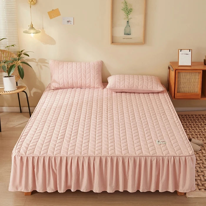 Pink quilted bedspread on a bed in a bedroom setting with a lamp and plant.