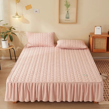 Pink quilted bedspread on a bed in a bedroom setting with a lamp and plant.