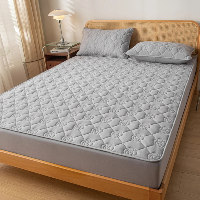 Gray quilted mattress cover on a wooden bed with pillows in a bedroom setting.
