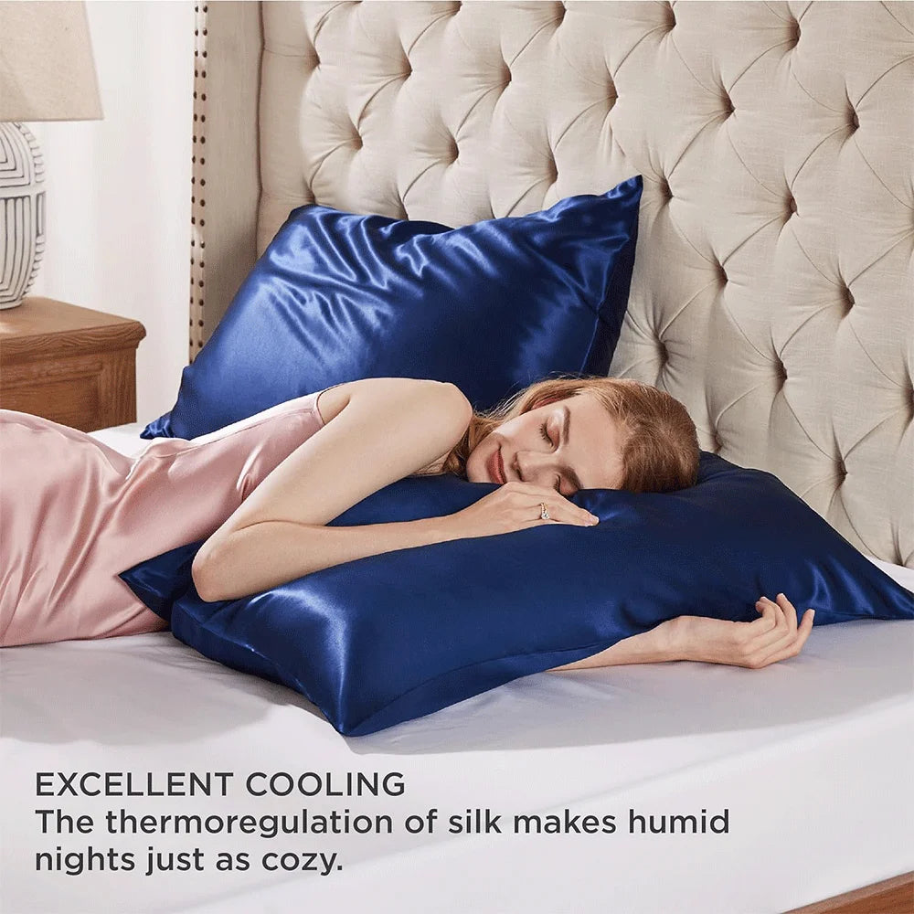 Woman lying on a bed with blue satin pillows, emphasizing comfort and cooling properties.
