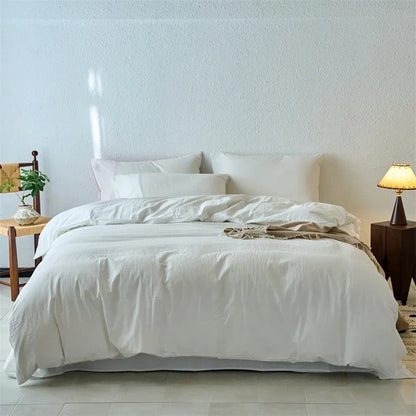 White bedding set on a bed in a minimalistic bedroom with a lamp and plant.