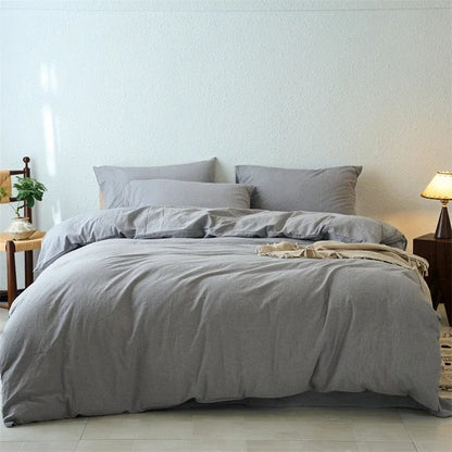 Gray bedding set on a bed in a bedroom with a lamp and plant.