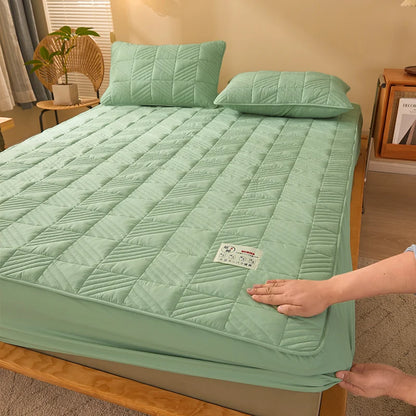 Green quilted mattress cover being adjusted on a bed in a bedroom setting.