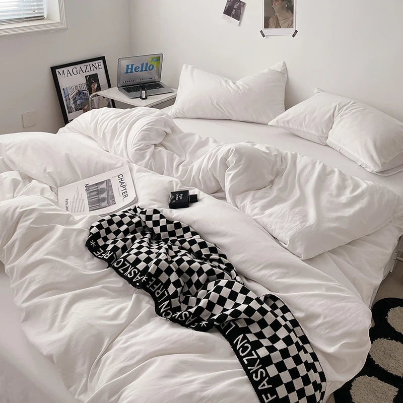 White comforter on a bed with a checkered blanket, laptop, and books in a room.