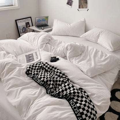 White comforter on a bed with a checkered blanket, laptop, and books in a room.