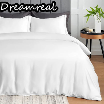 White bedding set on a bed with 'Dreamreal' branding, side table with decor items in the background.