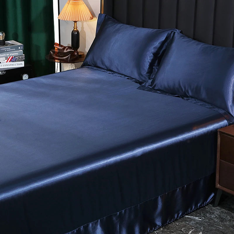 Navy blue satin sheet set on a bed with a lamp and books in the background.