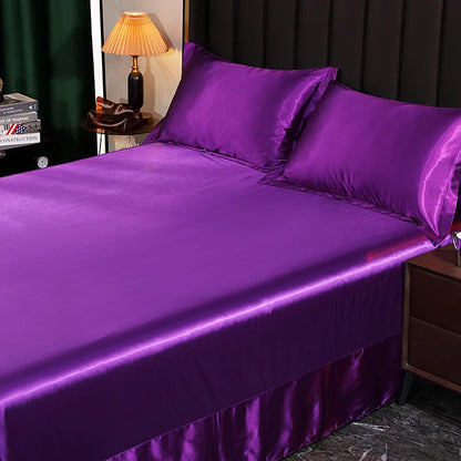 Purple satin bedding set on a bed with a lamp and books in the background.