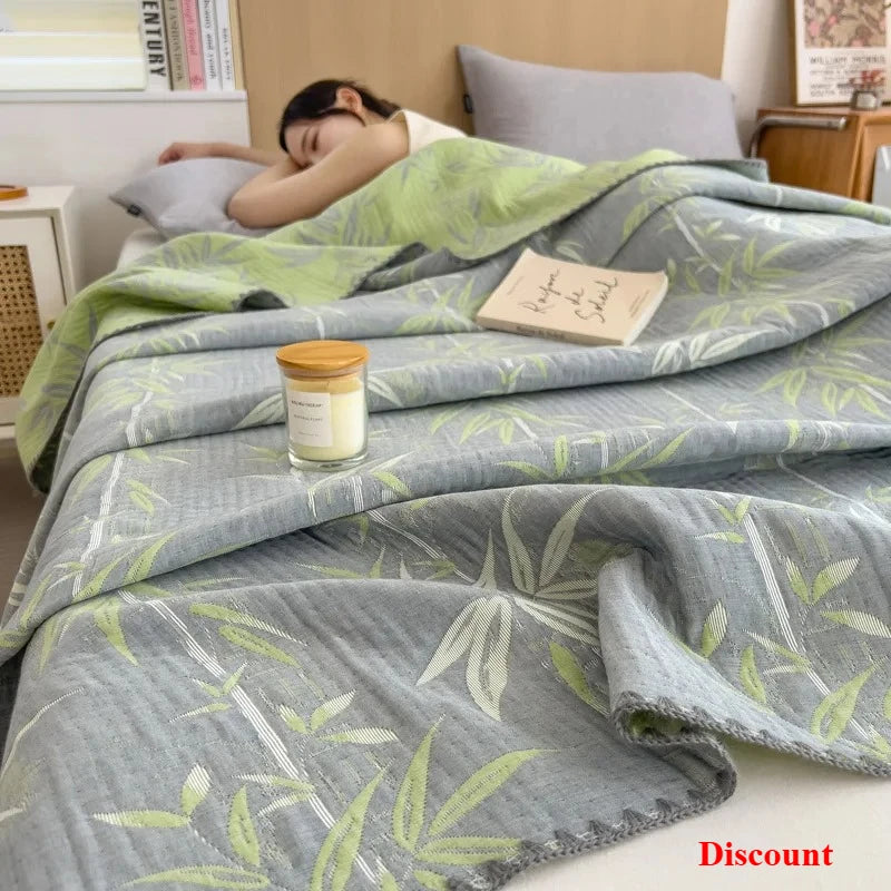 Person sleeping under a green and gray leaf-patterned blanket with a candle and book on a bed.