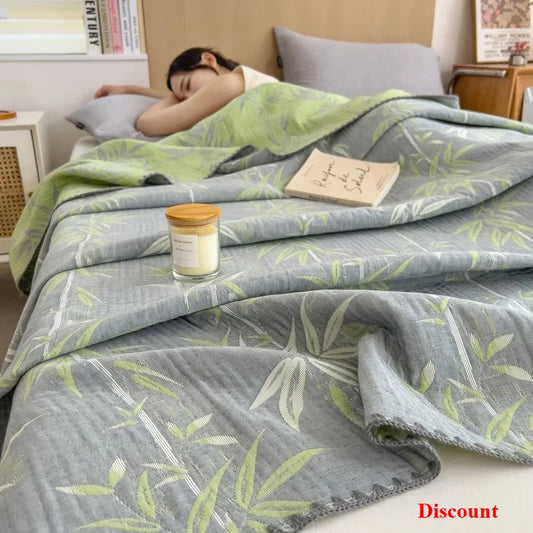 Person sleeping under a green and gray leaf-patterned blanket with a candle and book on a bed.