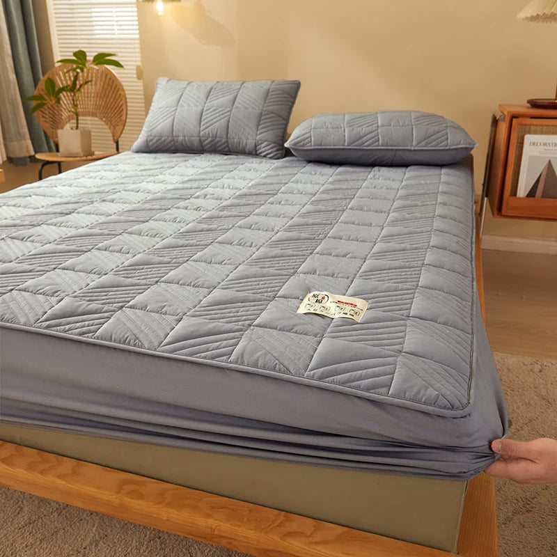 Gray quilted mattress cover on a bed in a bedroom setting