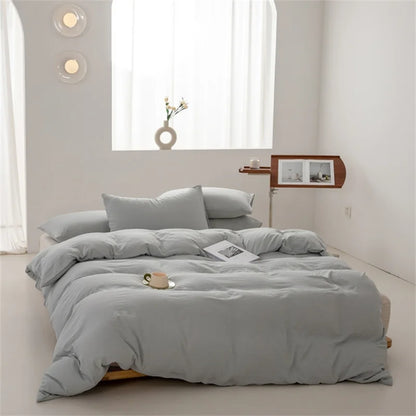 Gray bedding set on a bed in a minimalistic bedroom with a window and side table.