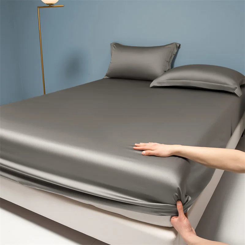 Person adjusting gray satin sheets on a bed against a blue wall.