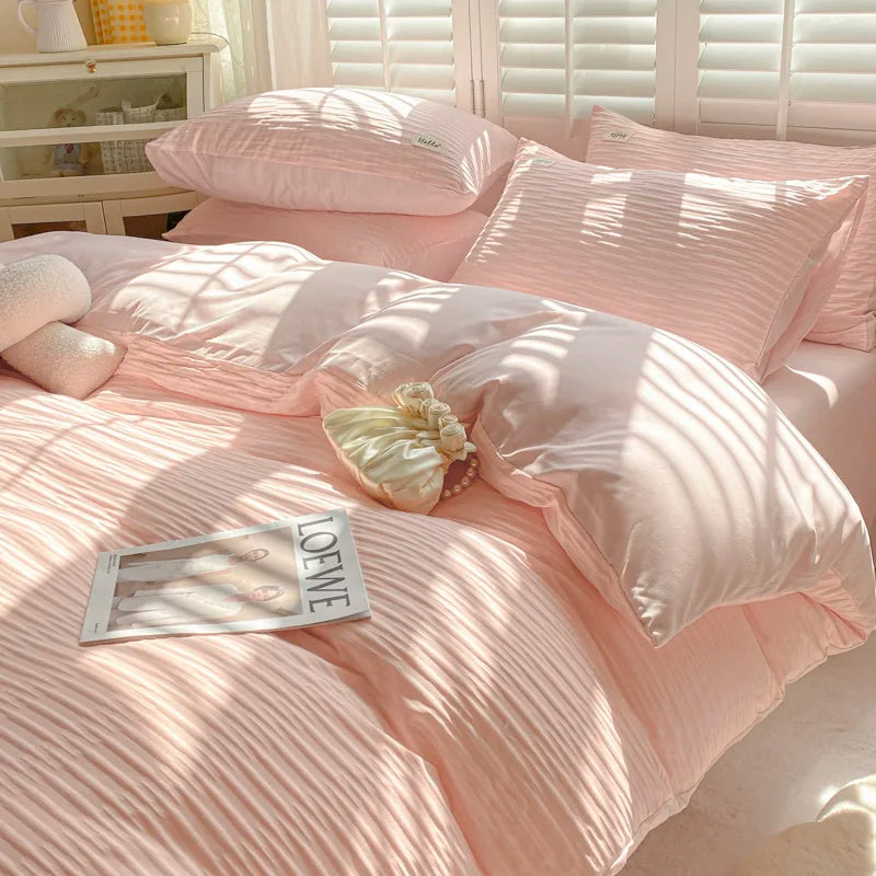 Pink striped bedding set on a bed with a magazine and decorative pillows.